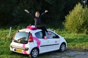 Een vrouw zit bovenop een roze auto met haar armen uitgestrekt en toont haar avontuurlijke geest en onbevreesde houding.