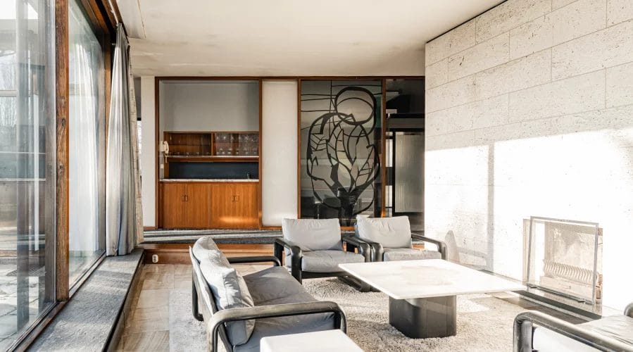 Een woonkamer met een open haard en grote raampartijen.