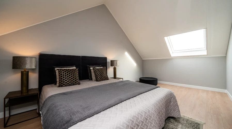 Een bed in een slaapkamer op zolder met een dakraam. meubels huren, meubelverhuur luxe pakket