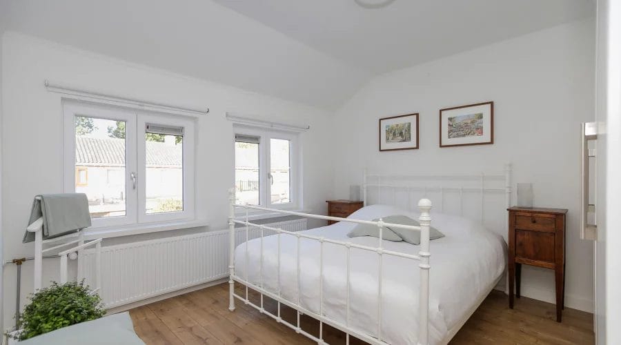 Een wit bed in een kamer met houten vloeren. verkoopstyling schiedam, neutrale inrichting, woningfotografie