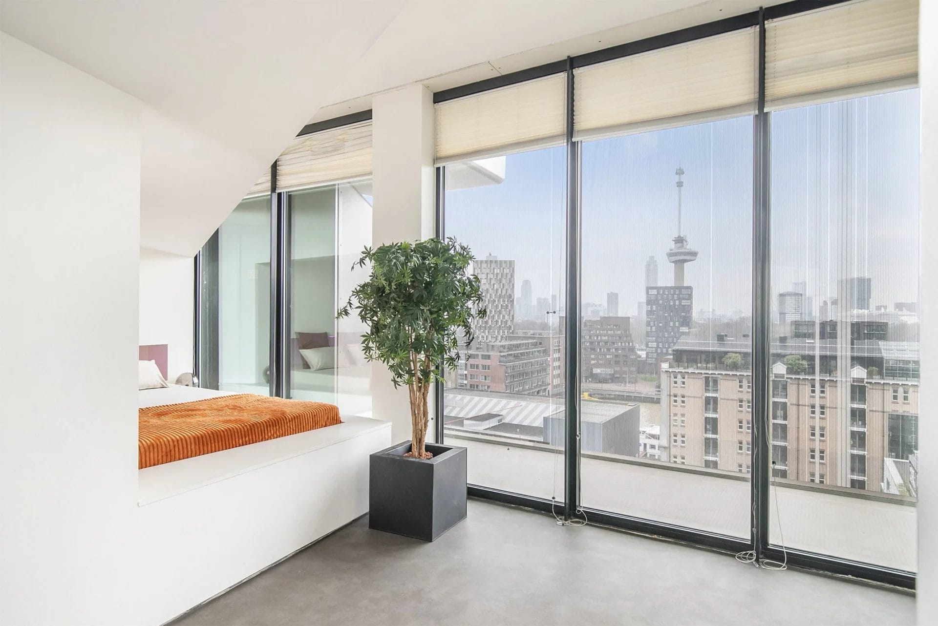 Een slaapkamer met grote ramen en uitzicht over de stad.