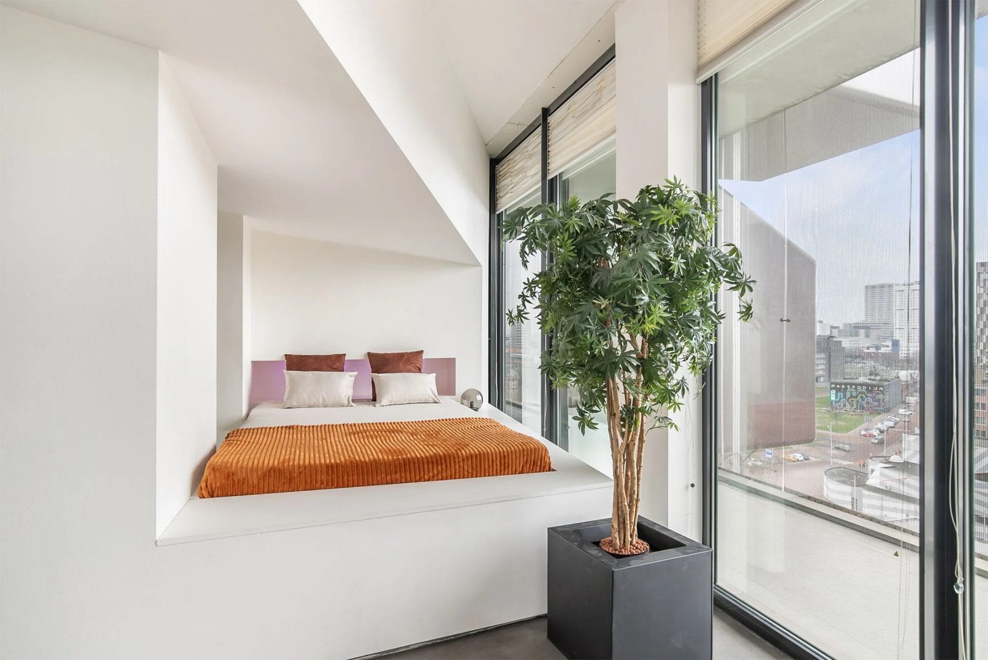 Een slaapkamer met een groot raam met uitzicht op een stad.